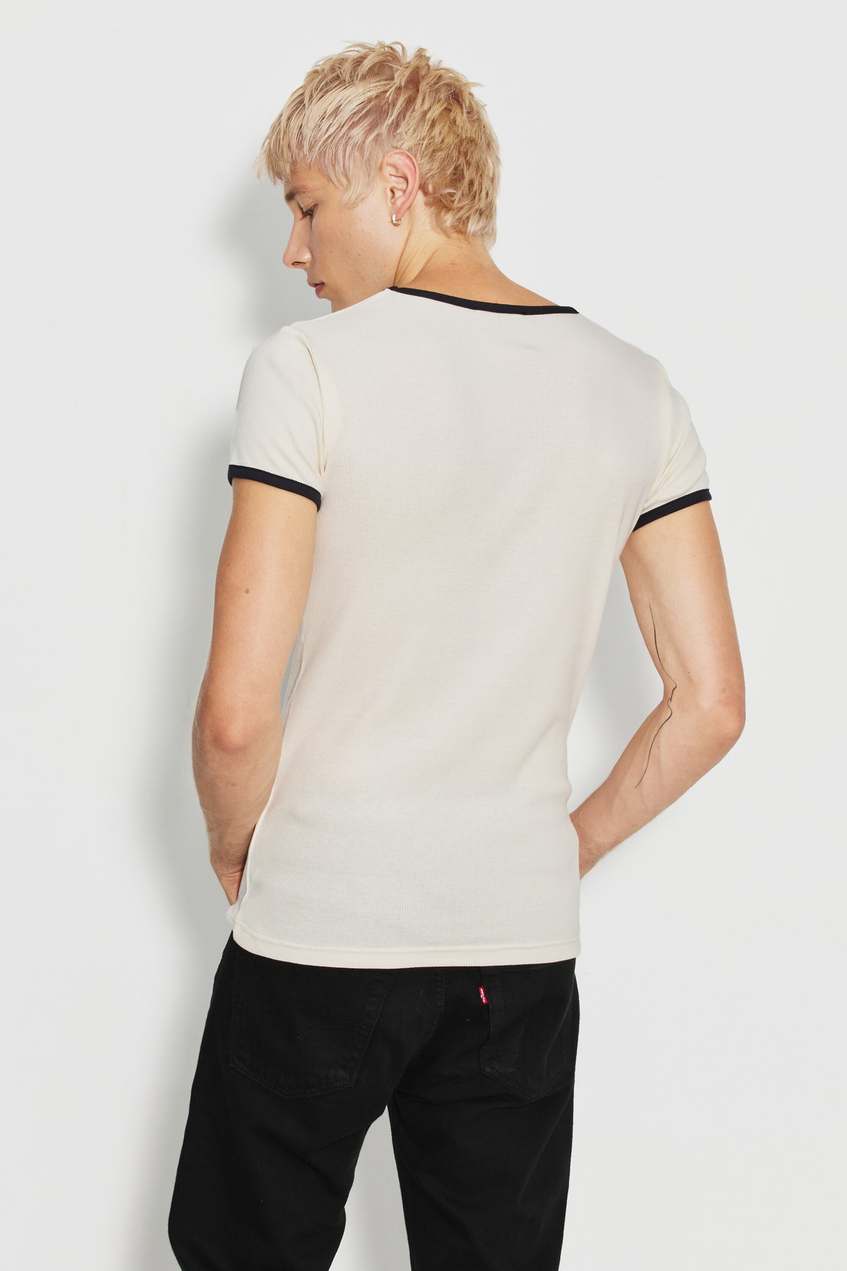 Maillot de corps homme bicolore écru et noir à manches courtes en coton Pima côtelé, porté de dos avec un pantalon noir, la tête tournée sur le côté.