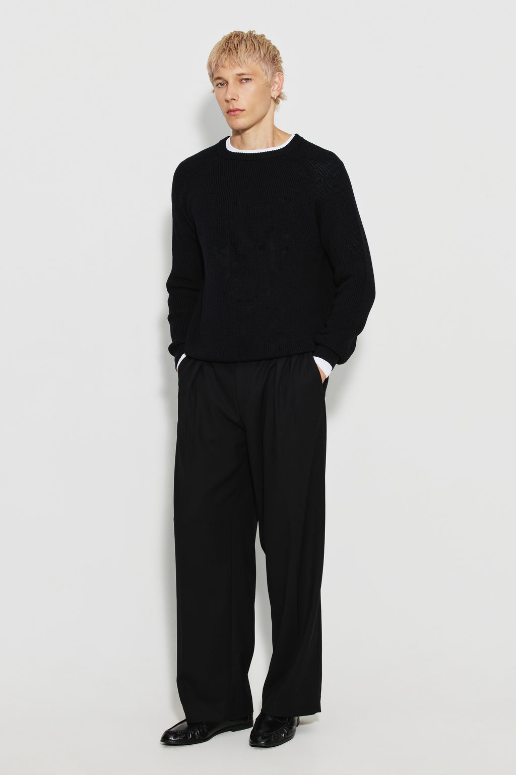 Pull homme noir en laine mérinos à manches raglan, porté avec un pantalon noir et des chaussures noires, vue de face en pied.
