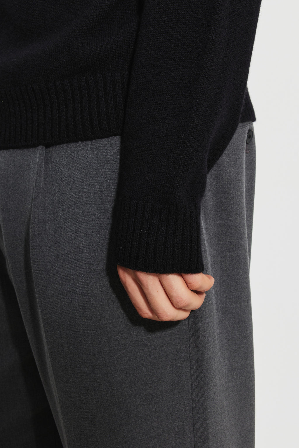 Pull mérinos et cachemire homme noir – détail du poignet et du bord-côte du bas, avec un pantalon gris.