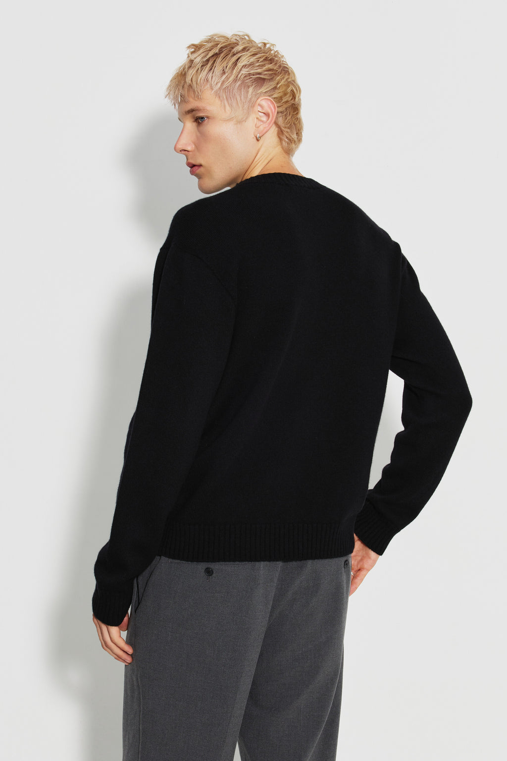 Pull mérinos et cachemire homme noir – vue de dos, la tête tournée de profil, avec un pantalon gris.