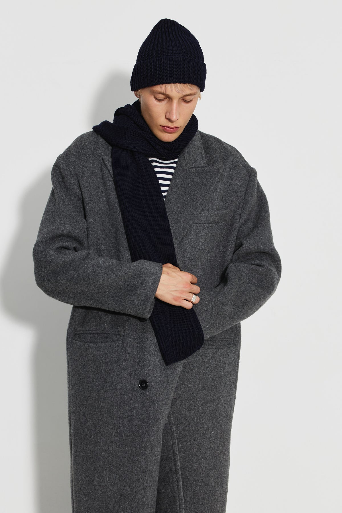Bonnet homme bleu marine en laine mérinos, porté avec un manteau gris et une écharpe bleu marine, la tête baissée.