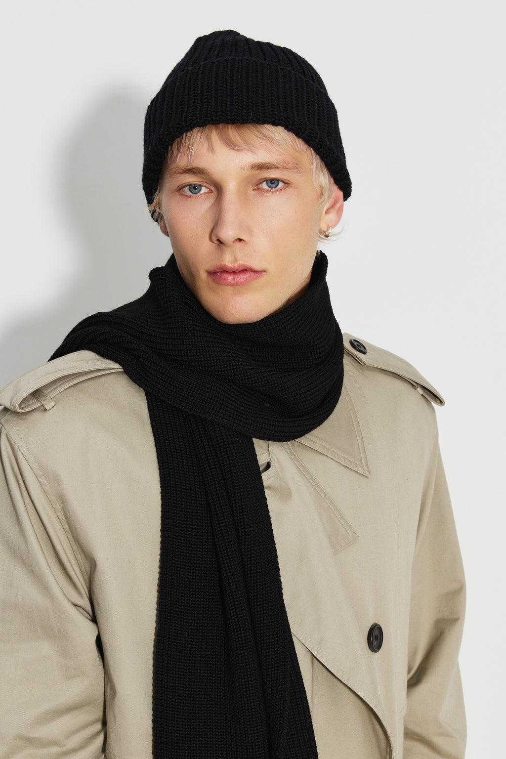 Bonnet homme noir en laine mérinos, porté avec une écharpe noire et un trench beige, vue de trois quarts.