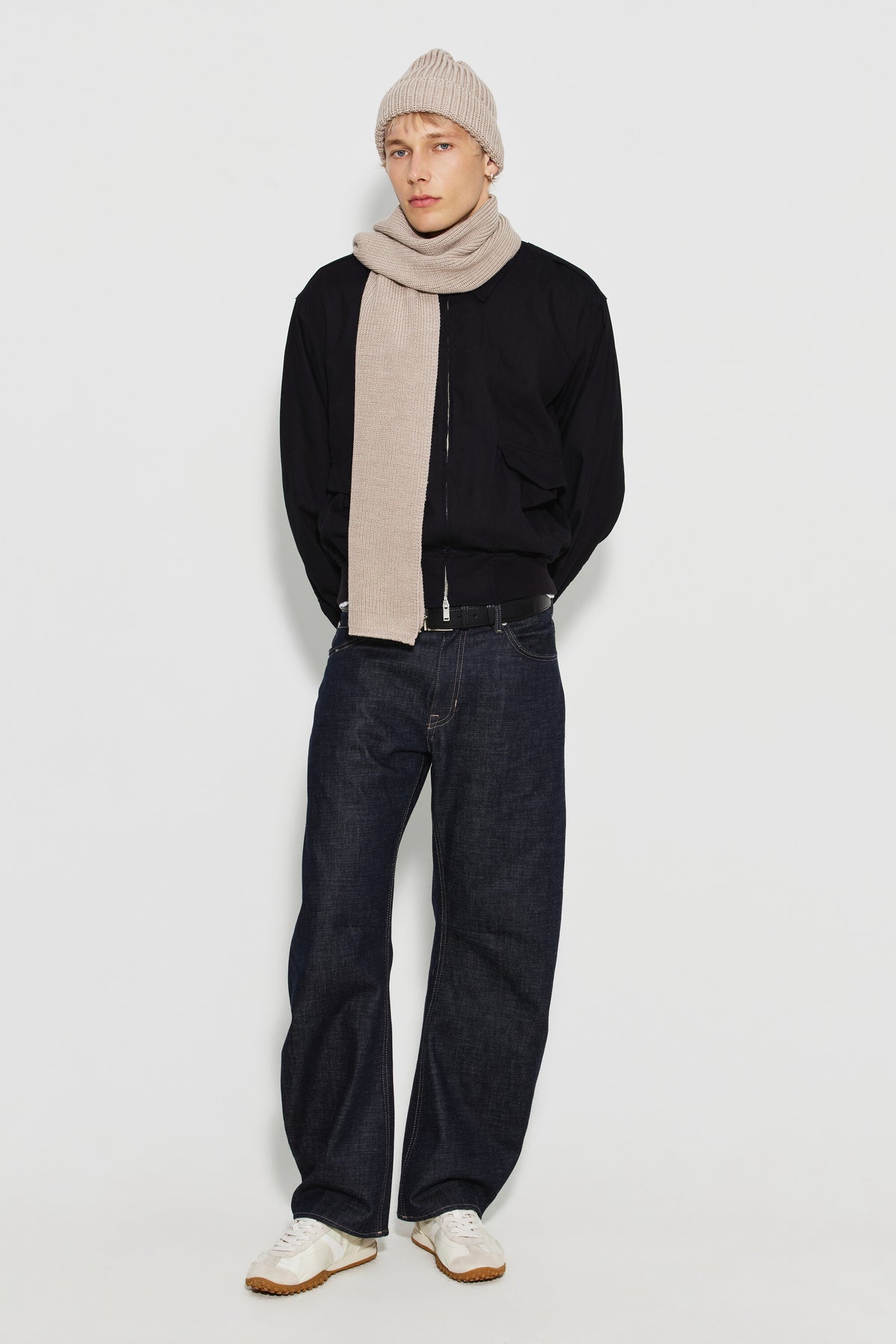 Écharpe homme beige en laine mérinos, portée avec un bonnet beige, un blouson noir et un jean foncé, vue de face en pied.