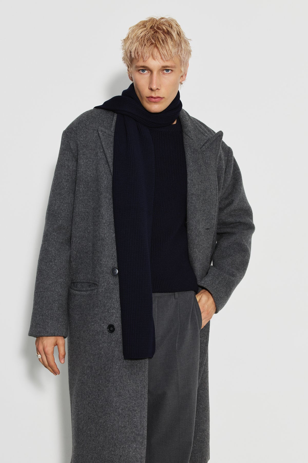 Écharpe homme bleu marine en laine mérinos, portée autour du cou avec un pan sur la poitrine et un manteau gris, vue de face. Made in France.
