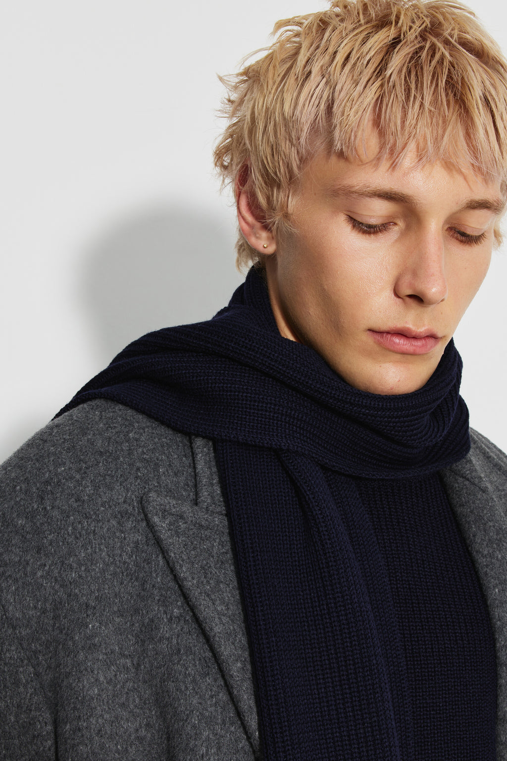 Écharpe homme bleu marine en laine mérinos, portrait rapproché montrant la maille de l’écharpe enroulée autour du cou, avec un manteau gris.