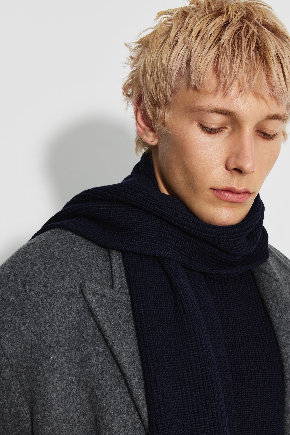 Écharpe homme bleu marine en laine mérinos, portrait rapproché montrant la maille de l’écharpe enroulée autour du cou, avec un manteau gris.
