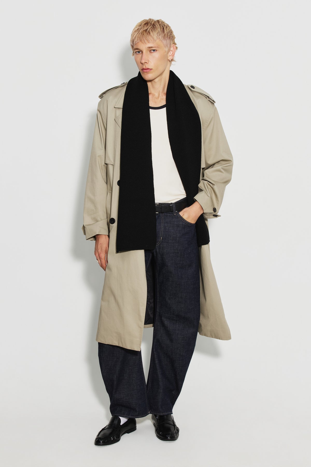 Écharpe homme noire en laine mérinos, portée longue autour du cou avec un trench beige et un jean foncé, vue en pied. Made in France.