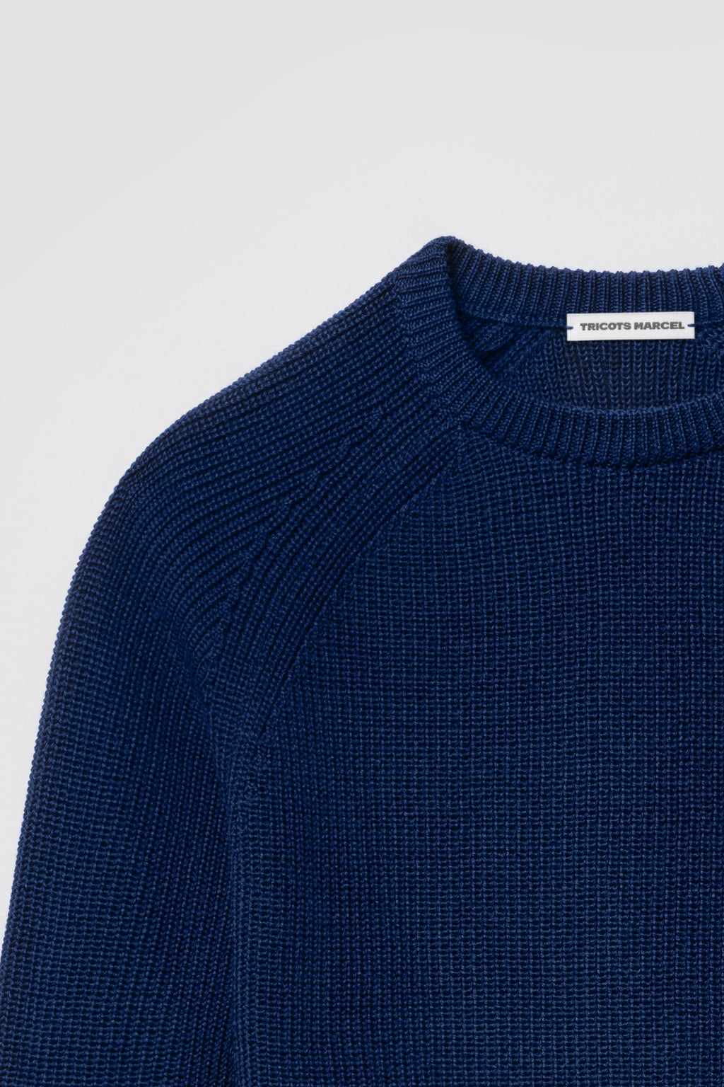 Pull bleu en laine mérinos à manches raglan, détail du col rond, de l’épaule raglan et de la maille perlée.