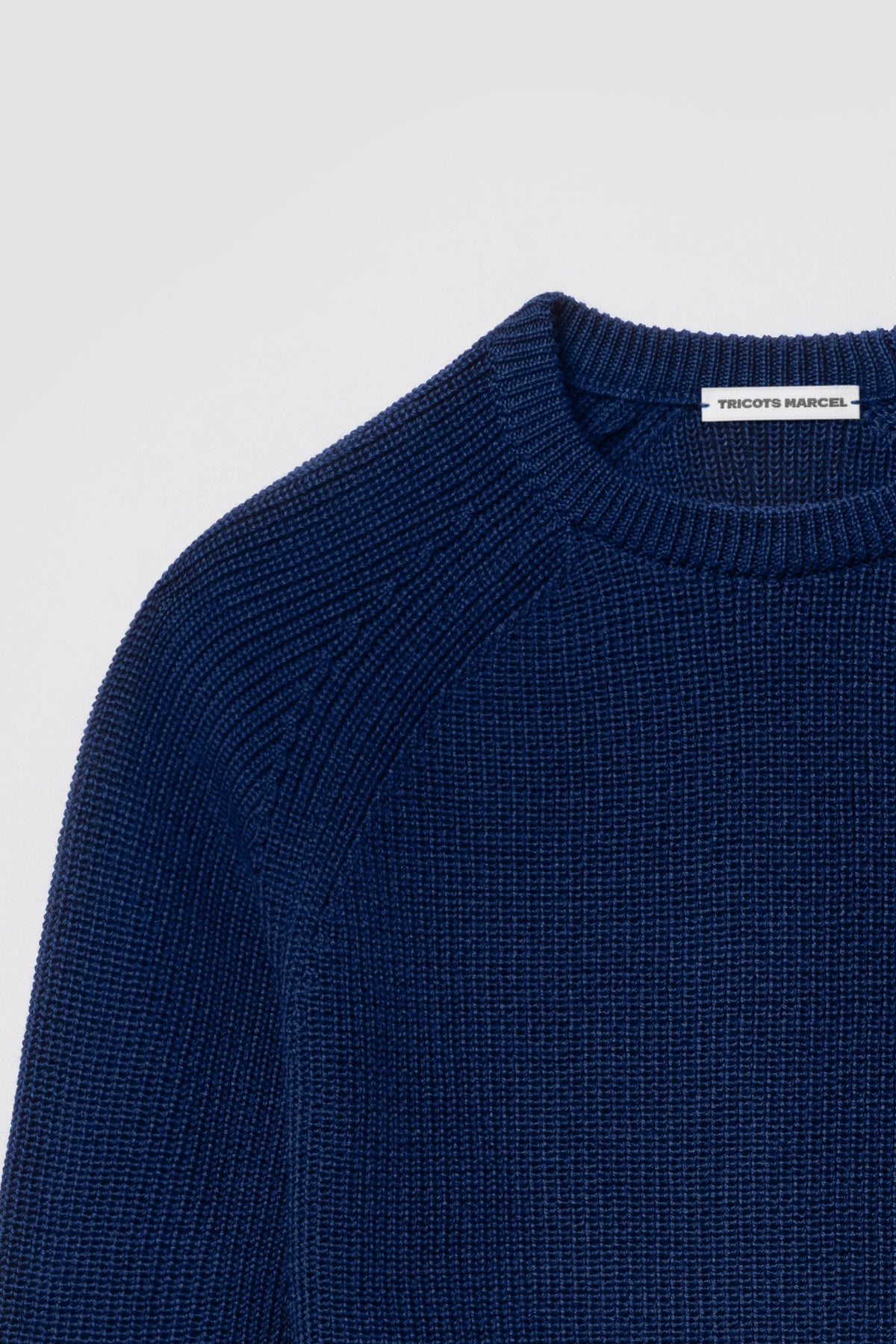 Pull bleu en laine mérinos à manches raglan, détail du col rond, de l’épaule raglan et de la maille perlée.
