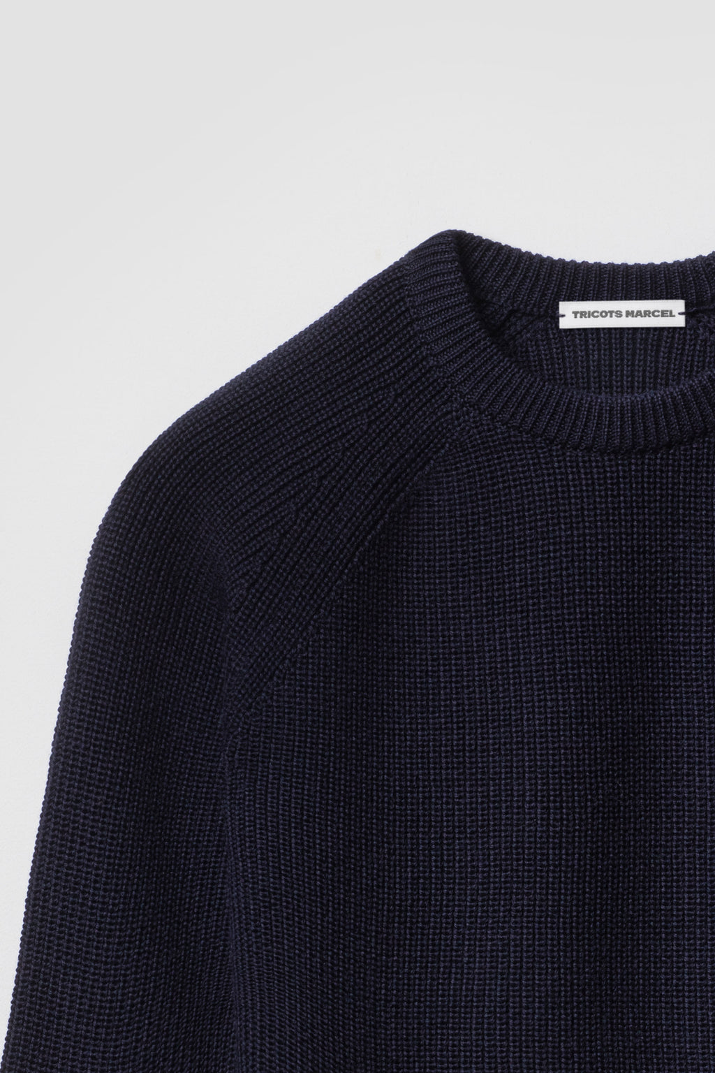 Pull homme et femme bleu marine en laine mérinos à manches raglan, détail du col rond, de l’épaule raglan et de la maille perlée. Made in France.