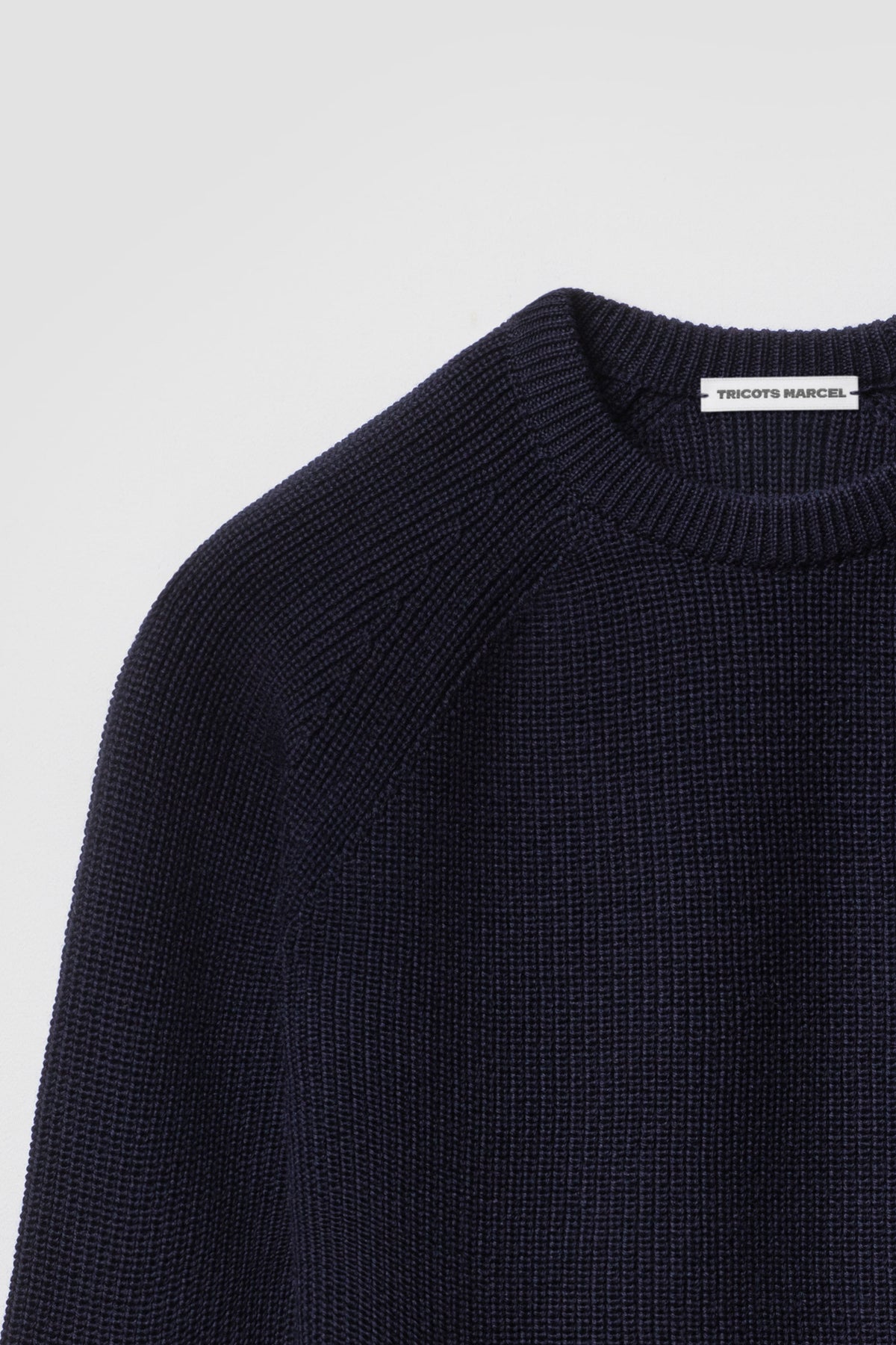 Pull homme et femme bleu marine en laine mérinos à manches raglan, détail du col rond, de l’épaule raglan et de la maille perlée. Made in France.