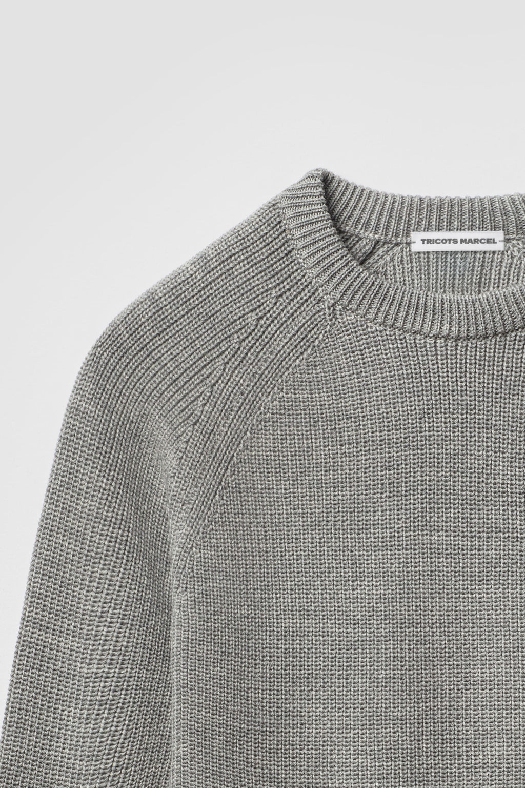 Pull gris en laine mérinos à manches raglan, détail du col rond, de l’épaule raglan et de la maille perlée.