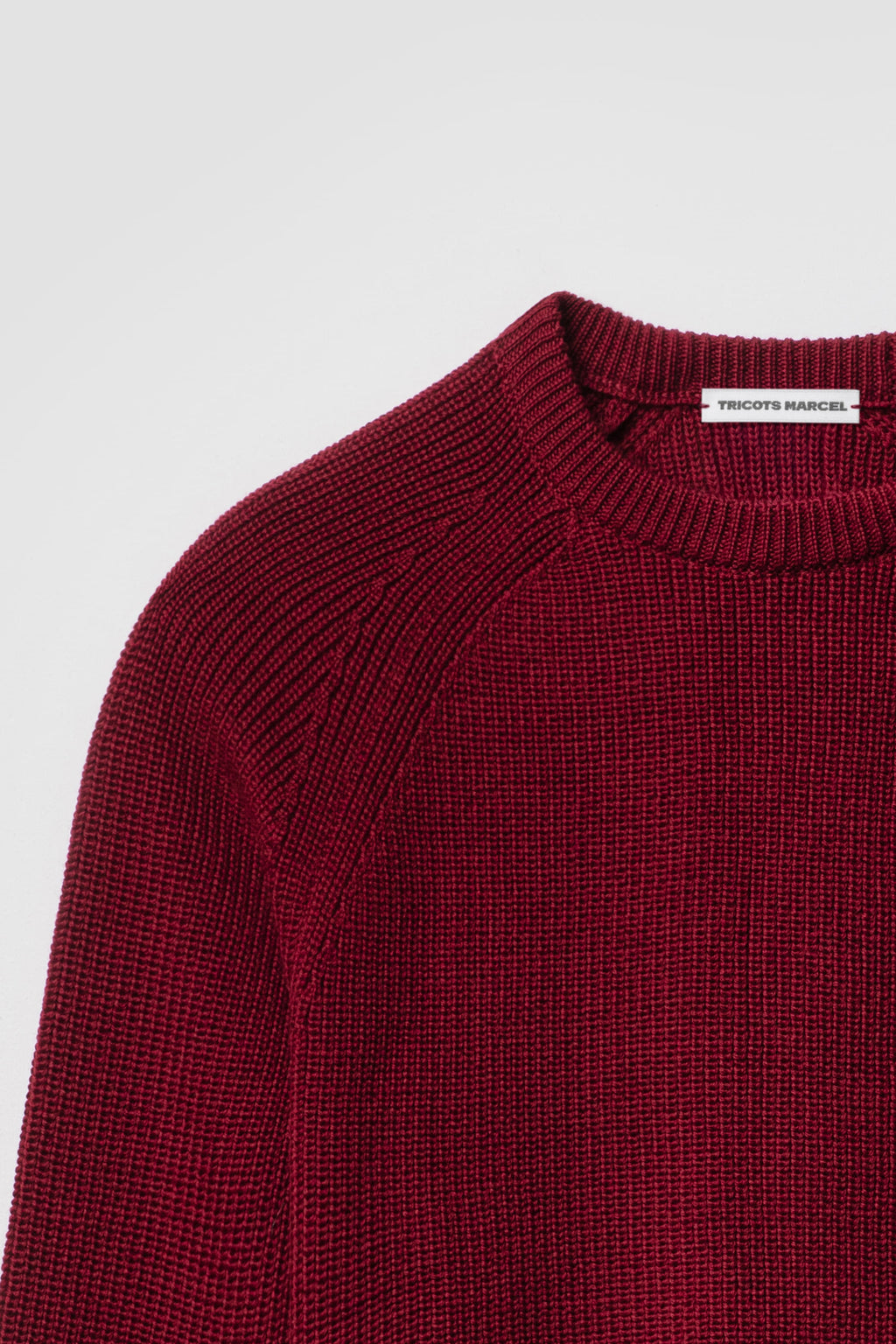 Pull rouge rubis en laine mérinos à manches raglan, détail du col rond, de l’épaule raglan et de la maille perlée.