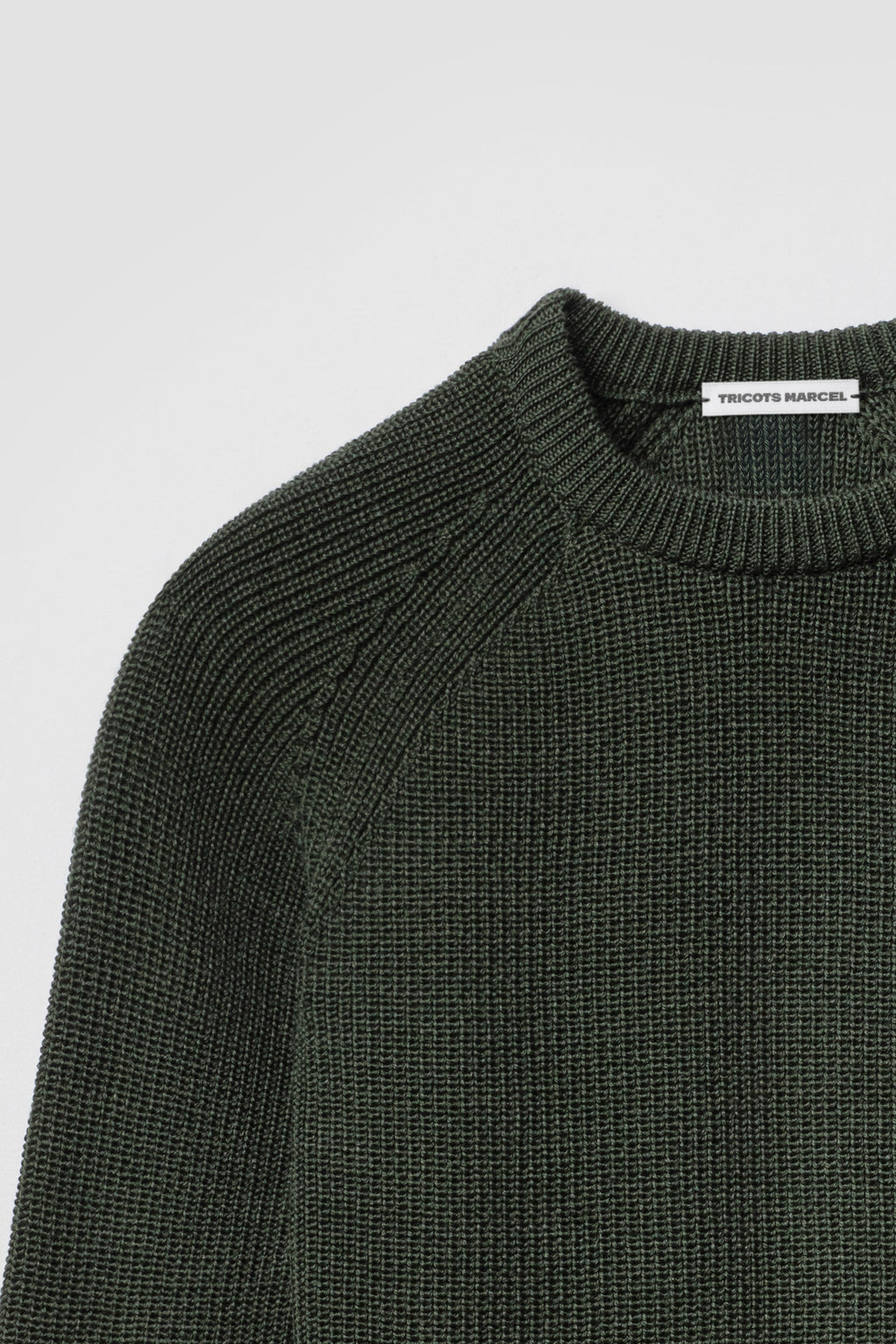 Pull vert kaki en laine mérinos à manches raglan, détail du col rond, de l’épaule raglan et de la maille perlée.